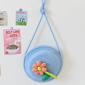 Détail d'un sac cabas tissé bleu clair avec une fleur orange 3D et une feuille verte