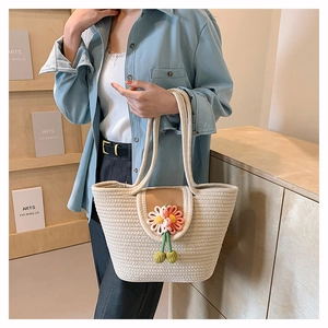 Detailed close-up of woven cream tote bag featuring a colorful 3D floral accent and tassels