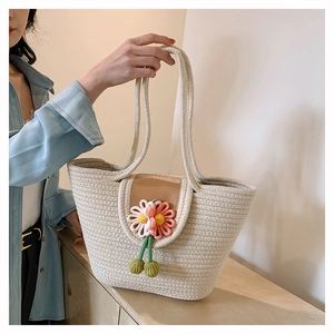 Detail of hand-woven straw tote with white daisy charms and green pom pom accents