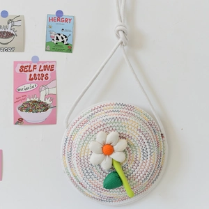 Détail d'un sac tissé rond avec des fleurs en tissu 3D et une bandoulière en coton blanc