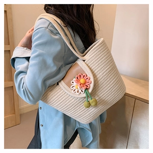 Detail view of woven straw tote bag with 3D floral accents and green round pendants