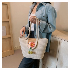 Detailed view of woven straw tote bag featuring a leather flap and daisy floral charm