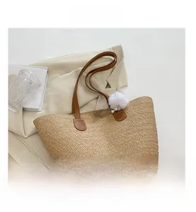 Détail d'un sac cabas en paille beige avec lanières en cuir marron et breloque