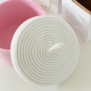 Dettaglio del cesto in corda di cotone rosa con coperchio bianco e trama intrecciata