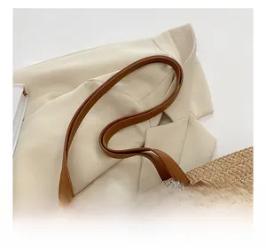 Détails des anses en cuir marron et du pompon décoratif sur un sac fourre-tout en paille tissée