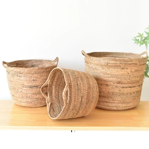 Detail of three nested woven seagrass baskets with dual handles on light wood surface