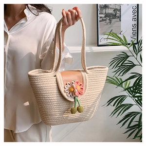 Detailed view of woven straw tote bag with floral accents and cherry decor on leather flap