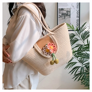 Detail view of woven straw tote bag with crochet flower and cherry decorations on white