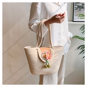 Detail of woven straw tote bag featuring orange leather flap and 3D daisy flower charm