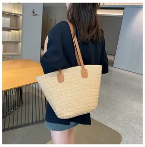 Détail du sac cabas en paille tissée avec anses en cuir marron porté à l'épaule