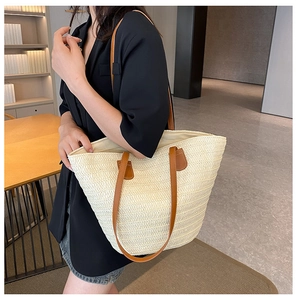 Détail d'un sac cabas en paille crème avec des anses en cuir marron pour la plage
