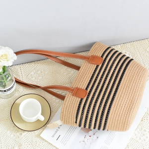 Close-up of beige woven straw tote bag with black stripes and brown leather handles