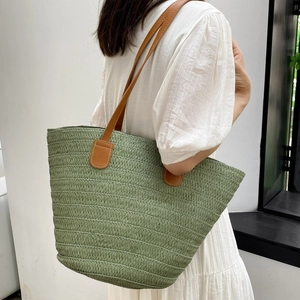 Sac cabas en paille tressée vert sauge avec anses en cuir marron porté par un mannequin pour l'été