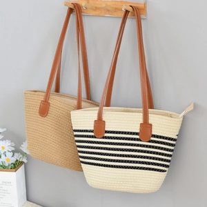 Detail of straw tote bag showing brown leather handles and secure zipper closure detail