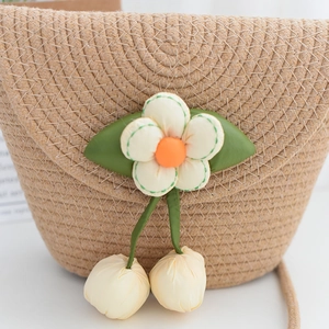 Détail d'un sac à bandoulière en paille tressée avec fleurs et breloques cerises