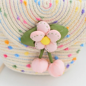 Détail d'un sac à bandoulière en paille avec pompons colorés et décoration florale