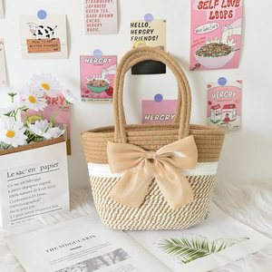 Detail of hand-woven cotton striped tote bag featuring a large satin bow on white fur rug