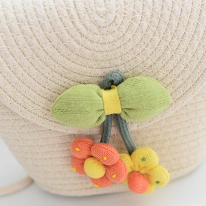 Détail d'un sac en paille tressée avec fleurs en tissu et nœud papillon vert
