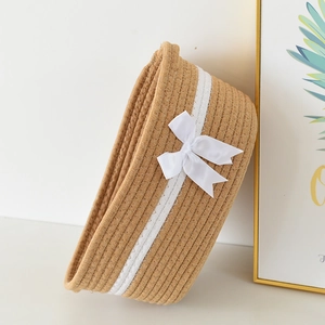 Detailed close-up of a woven cotton rope storage basket with a white satin bow accent