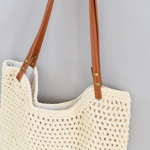 Detail of hand-woven straw tote bag with brown leather strap and gold rivet accents