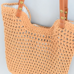 Detail showing orange woven texture, brown leather handle and gold studs on a tote bag
