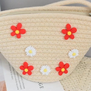 Detail of straw woven purse featuring 3D daisy flower decorations and zip closure