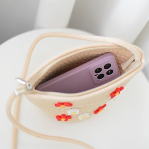 Detail of straw crossbody bag showing internal capacity with phone and daisy decor