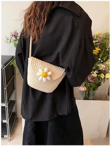 Detail of hand-woven beige straw crossbody bag with daisy flower on a female model