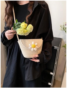 Detailed shot of beige woven crossbody bag with 3D white daisy flower on black shirt