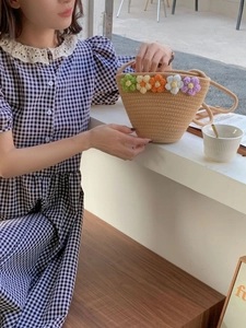 Detail of a handmade woven bucket bag with crochet flower accents on a model in a cafe