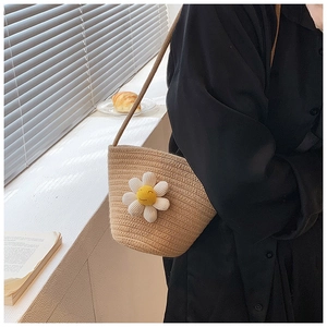 Close-up of handwoven straw bag featuring a small daisy charm with smile face embroidery