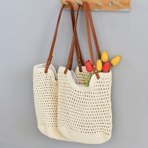Close-up of woven straw beach tote bag with brown leather straps and metal rivets detail