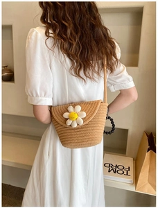 Close-up of a woven straw crossbody bag with a white daisy floral applique and slim strap