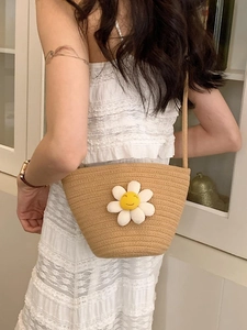 Detailed view of woven straw bucket bag with white sunflower and crossbody strap worn by model