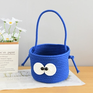 Detail of blue cotton woven basket with cute big eye design and decorative tassel accent