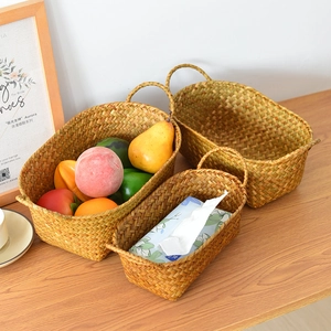 Three-piece set of oval handmade woven straw storage baskets with dual handles on wood surface