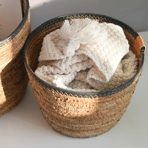 Detail of woven straw storage basket with brown leather handle and white tassel blanket