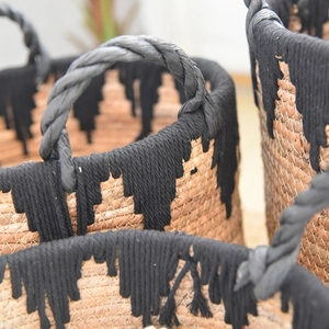 Detail of woven straw basket featuring black fringe accents and sturdy braided handles