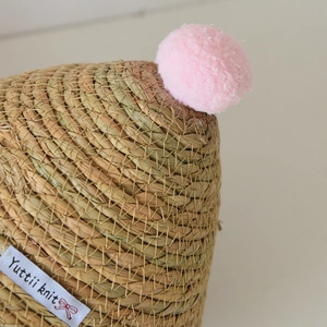Dettaglio della trama in cotone intrecciato con pompon rosa ed etichetta su cesto portaoggetti