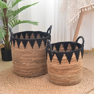 Detail of two-piece bohemian grass woven storage baskets with black handles and tassels