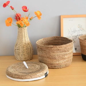 Detail of round seagrass storage basket with white rim handle and woven flower vase