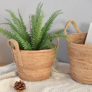 Nordic woven plant basket with dual handles and green plants on a white cozy blanket