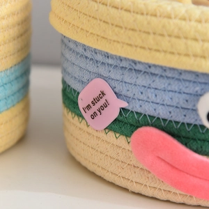Detail of multi-color woven cotton storage basket with cute cartoon eye and text tag