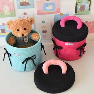 Detail of woven cotton storage basket with round lid, bow accent, and cute bear inside