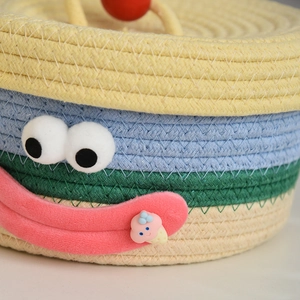 Detailed close-up of a colorful woven storage basket with cute cartoon plush eyes and mouth