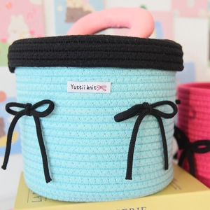 Detail of woven cotton storage basket showing pink handles and blue knitted texture