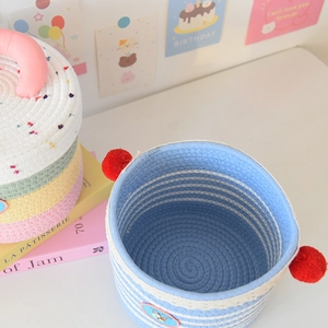 Close-up of woven cotton rope storage basket with blue stripes and red pom-poms detail