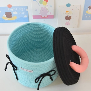 Close-up of a light blue woven storage basket with pink handle and a black lid