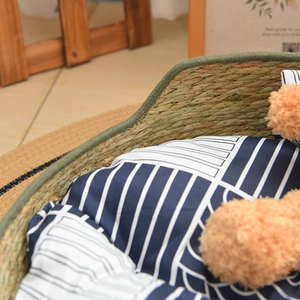 Detailed close-up of handmade woven straw pet bed with blue striped soft cushion and toy