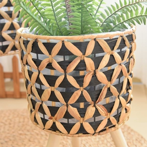Close-up of woven flower pot with black diamond pattern and natural wooden tripod legs